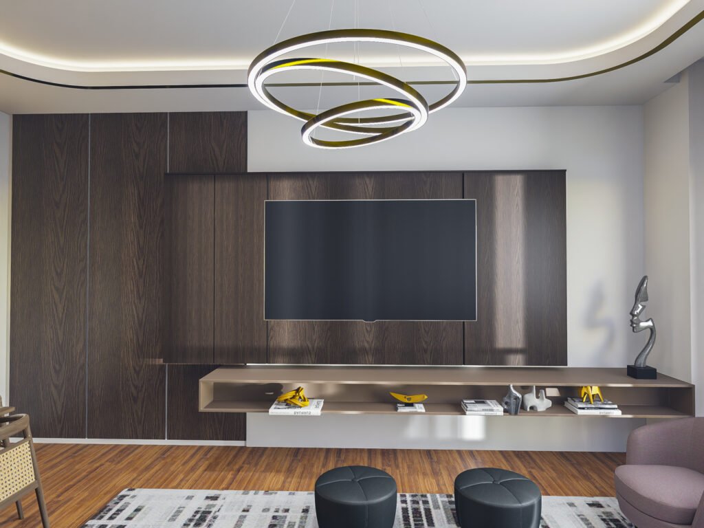 Koyu ahşap TV duvar ünitesi tasarımı, modern halka LED avize, siyah deri puflar ve gold detaylı dekoratif aksesuarlar.